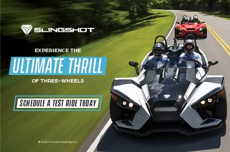 A white and a red Slingshot driving down a highway. Experience the ultimate thrill of three-wheels. Schedule a test ride today.