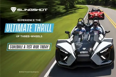 A white and a red Slingshot driving down a highway. Experience the ultimate thrill of three-wheels. Schedule a test ride today.